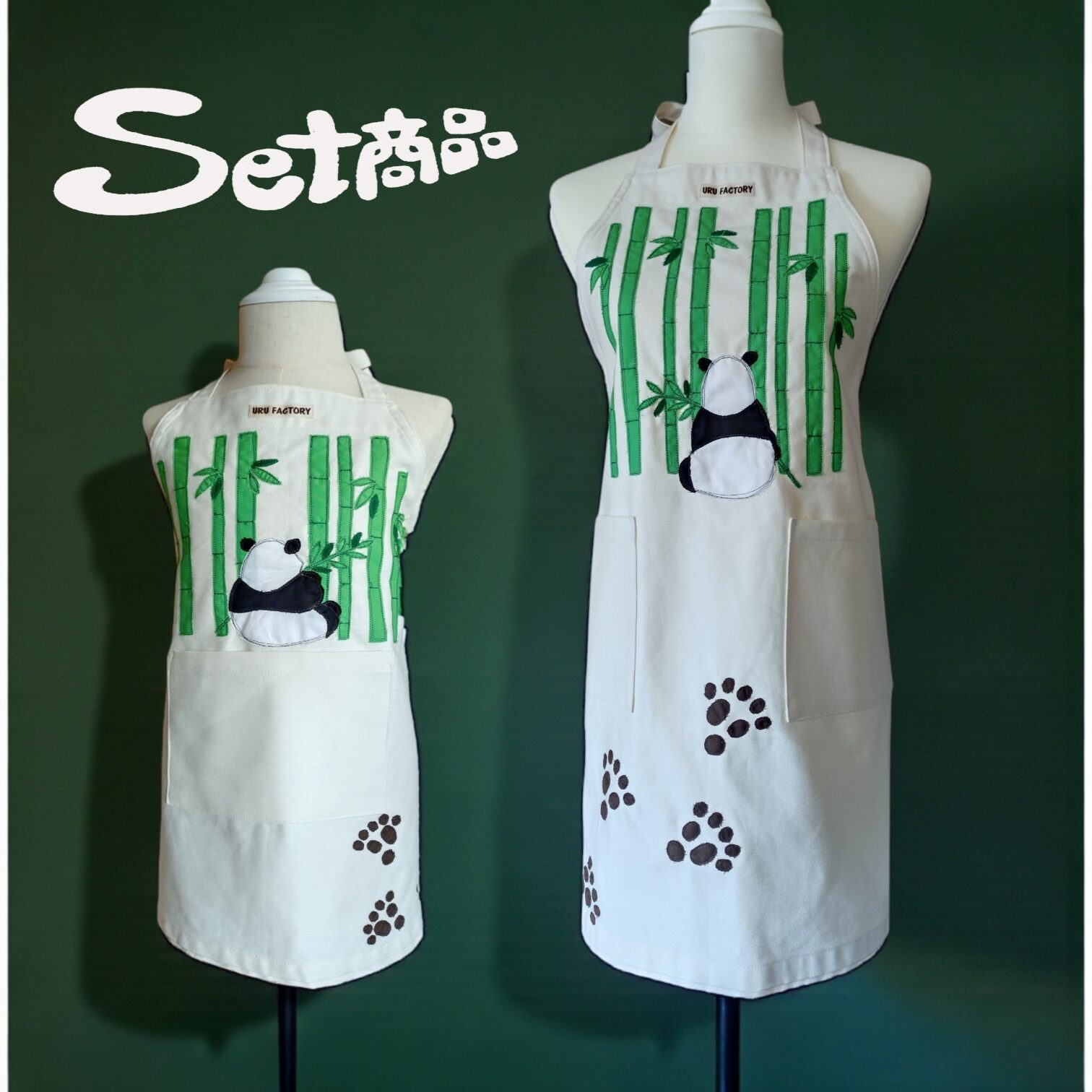 竹藪の前に座るパンダの後ろ姿と足跡のアップリケを配した親用と子供用エプロン