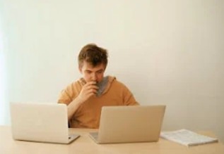 2つのパソコンを前にして考え込む人
